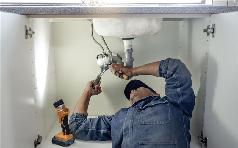 Plumber repairing pipes beneath a bathroom sink in Wheat Ridge