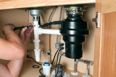 Plumber repairing a garbage disposal beneath a kitchen sink in Wheat Ridge
