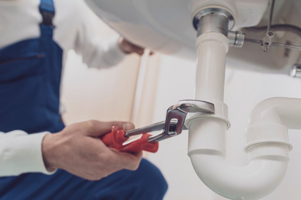 Plumber repairing a white drain pipe beneath a sink in Wheat Ridge