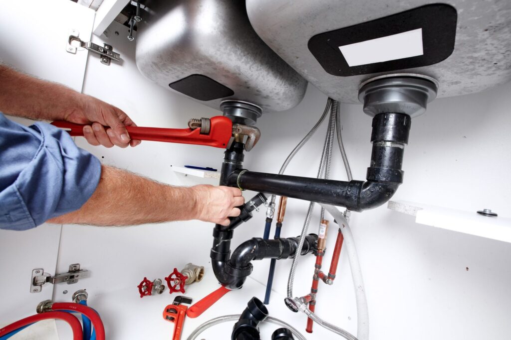 Plumber repairing drain pipes beneath a kitchen sink in Wheat Ridge